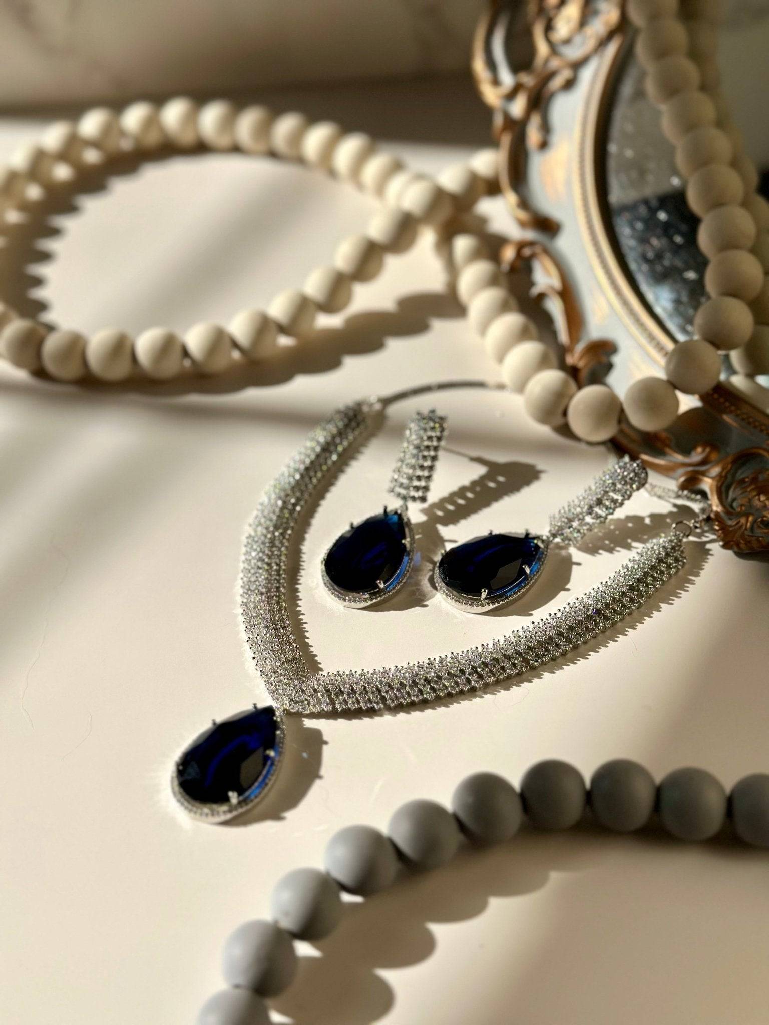Sharmine Paved Silver Diamanté Accent Necklace Set - Rhodium-plated with Diamanté stones, featuring a large teardrop stone and chandelier earrings, available in multiple color options, perfect for modern South Asian ensembles.