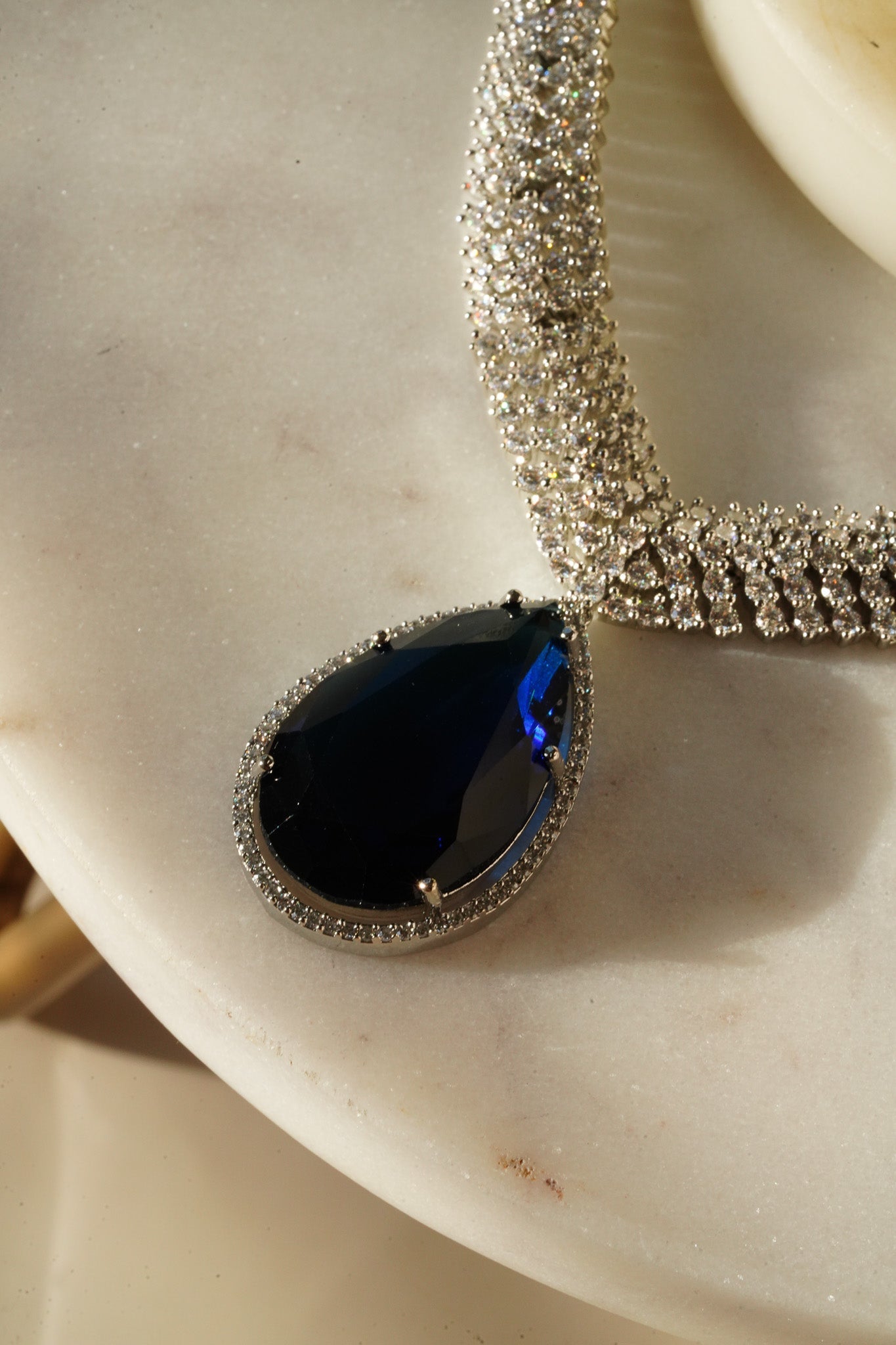 Sharmine Paved Silver Diamanté Accent Necklace Set - Rhodium-plated with Diamanté stones, featuring a large teardrop stone and chandelier earrings, available in multiple color options, perfect for modern South Asian ensembles.